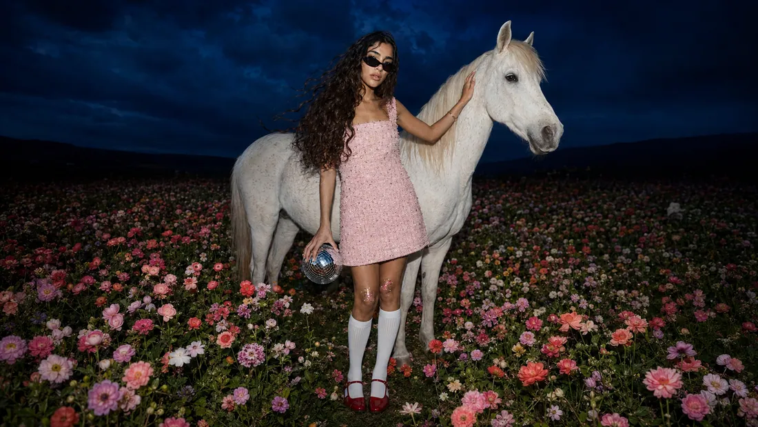 Woman in a pink dress beside a white horse in a field of flowers